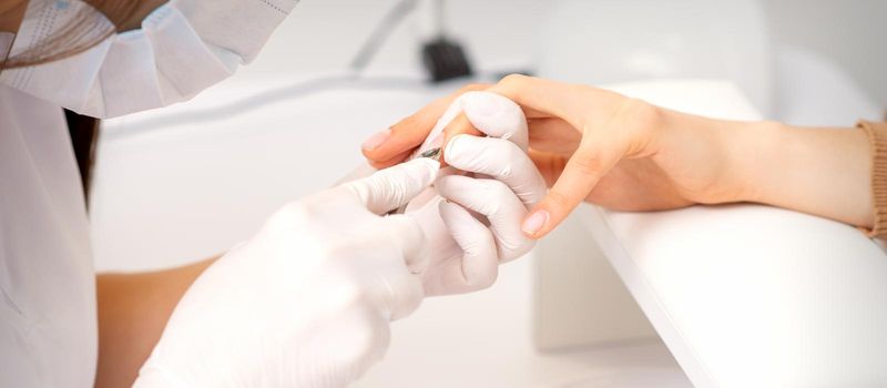 Close up of manicure master with manicure nipper cuts cuticles of female nails at beauty salon