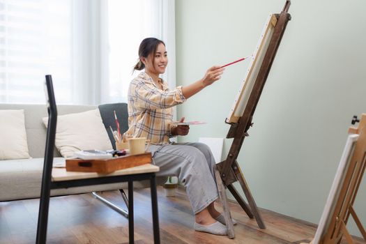 Joyful young female artist painting on canvas at workshop.