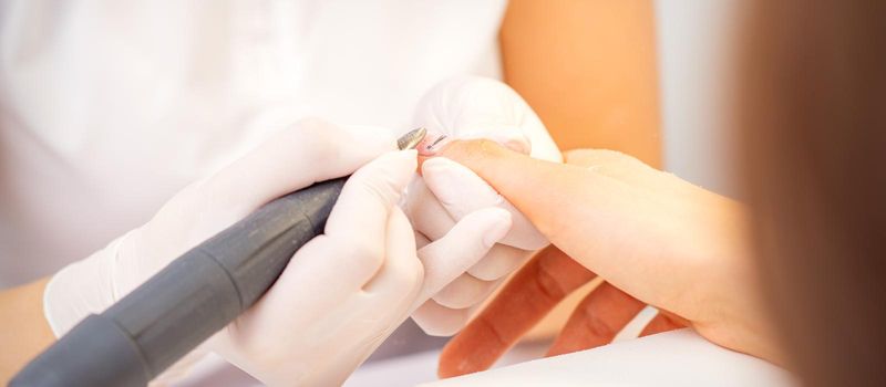 Closeup of manicure master in white gloves applying an electric nail file drill to remove the nail polish in the beauty salon