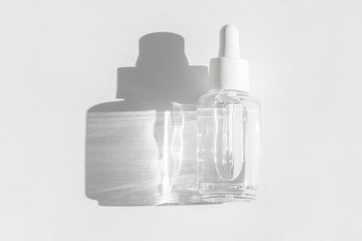Anti aging serum with collagen and peptides on white with sunlight and shadow. Hyaluronic or polyglutamic acid oil cosmetic mockup. Transparent liquid product packaging in glass bottle. Flat lay