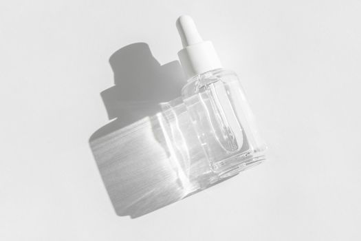 Transparent liquid product packaging in glass bottle. Anti aging serum with collagen and peptides on white with sunlight and shadow. Hyaluronic or polyglutamic acid oil cosmetic mockup. Flat lay.