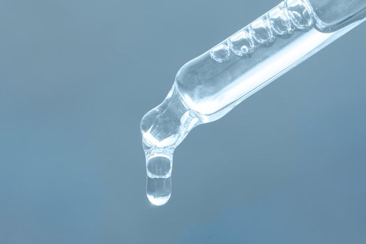 Beauty skin care product. Pipette with essential oil, serum with peptides, hyaluronic acid on blue background. Closeup of blue dropper, falling drop close up. Self care concept