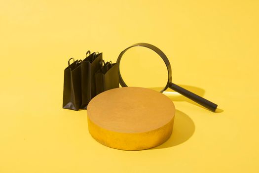 Empty mockup podium or pedestal and miniature black shopping bags and magnifire in black friday sale on yellow background.