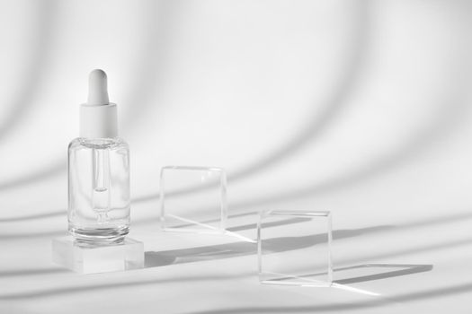 Serum cosmetic bottle mockup on acrylic transparent solid block pedestal on white background, shadow from sun, natural light from windows. Geometric stand, podium for cosmetics, product presentation