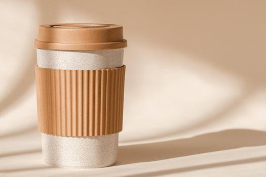Sustainable bamboo eco friendly cup with silicone holder on natural shadow beige background. Reusable, biodegradable travel plastic coffee mug for take away. Zero waste, sustainability concept.