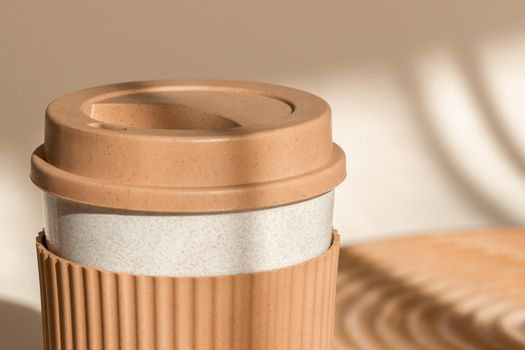 Reusable cup, biodegradable travel plastic coffee mug take away. Bamboo eco friendly cup on natural shadow beige background. Zero waste, sustainability concept. Close up view, sustainable lifestyle