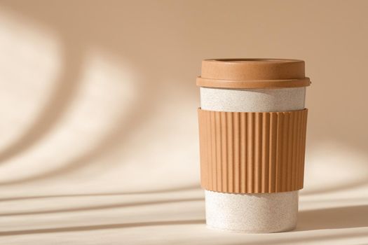 Reusable cup, biodegradable travel plastic coffee mug for take away. Sustainable bamboo eco friendly cup with silicone holder on natural shadow beige background. Zero waste, sustainability concept.