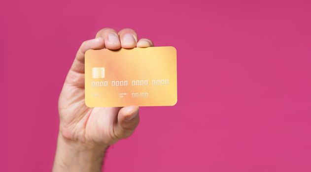 Close up yellow debit, credit card in man hand isolated on pink background. Financial, banking concept. No face visible.