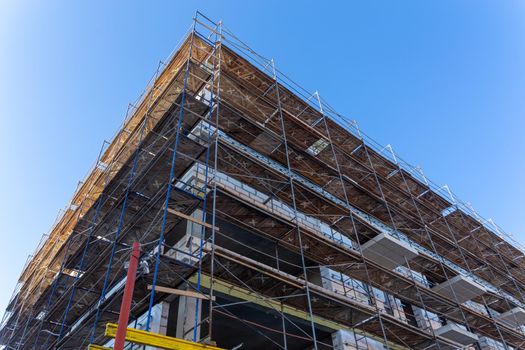 Insulation of the exterior walls of a building under construction. The walls of the building under construction are surrounded by scaffolding for workers to access. Exterior finishing works.