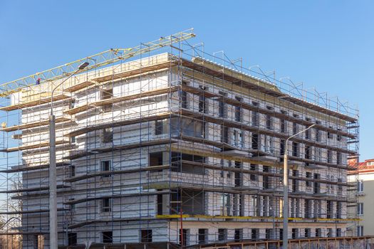 Insulation of the exterior walls of a building under construction. The walls of the building under construction are surrounded by scaffolding for workers to access. Exterior finishing works.