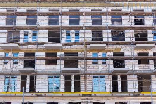 Insulation of the exterior walls of a building under construction. The walls of the building under construction are surrounded by scaffolding for workers to access. Exterior finishing works.