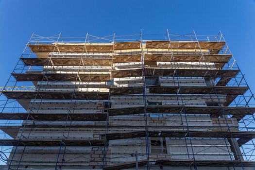 Insulation of the exterior walls of a building under construction. The walls of the building under construction are surrounded by scaffolding for workers to access. Exterior finishing works.