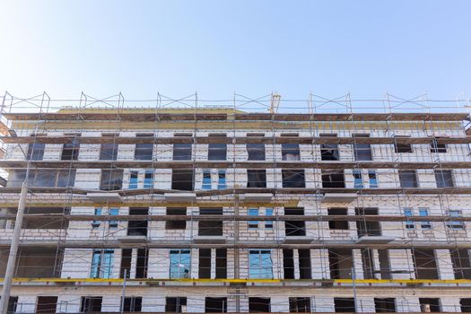 Insulation of the exterior walls of a building under construction. The walls of the building under construction are surrounded by scaffolding for workers to access. Exterior finishing works.