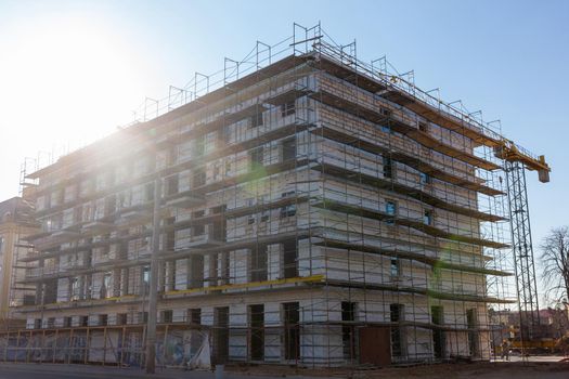 Insulation of the exterior walls of a building under construction. The walls of the building under construction are surrounded by scaffolding for workers to access. Exterior finishing works.