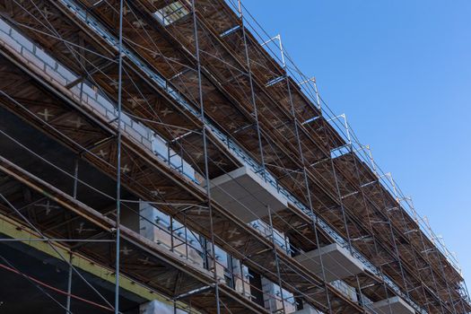 Insulation of the exterior walls of a building under construction. The walls of the building under construction are surrounded by scaffolding for workers to access. Exterior finishing works.