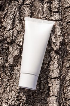 Beauty product packaging mockup. Organic cosmetic cream in tube on a tree bark natural background. Cream bottle, lotion, mousse, shampoo for skincare routine.