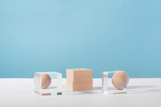 Wooden and glass cube podium and wooden sphere on blue background for product advertising, front view. Creative product stage mock up, cosmetic display platform or cosmetics showcase, geometric stand.