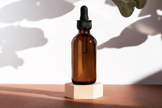 Amber serum cosmetic bottle on wooden geometric pedestal podium, product packaging with natural shadows from plants, anti aging serum with peptides, cosmetics mockup, skincare concept. Front view