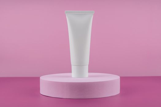 White tube of cosmetic product on podium pedestal on pink background. Cream bottle, lotion, mousse showcase for skincare routine. Beauty cleanser, shampoo stand. Sunscreen presentation mock up