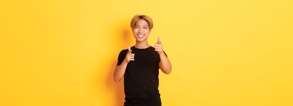 Portrait of cheeky smiling asian guy, looking satisfied and pointing fingers at camera, praising something or making compliment.