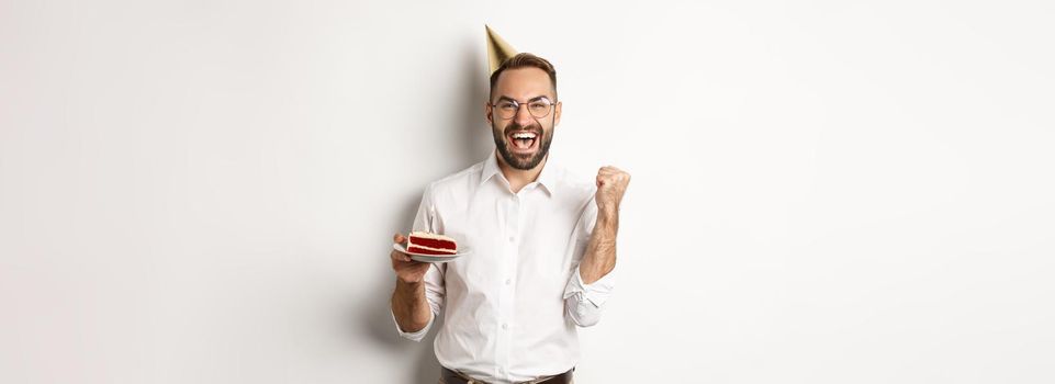 Holidays and celebration. Birthday guy making wish on bday cake and rejoicing, making fist pump sign as winning, achieve goal, white background.