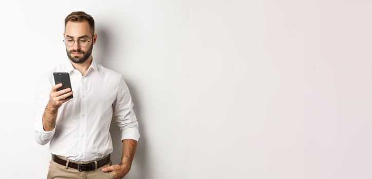 Businessman reading message on phone, standing over white background.