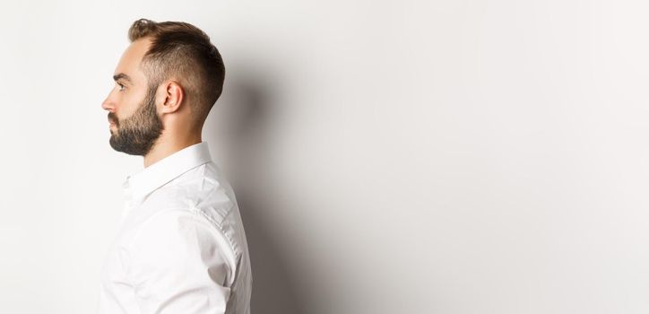 Close-up profile shot of handsome bearded man looking left, standing against white background.