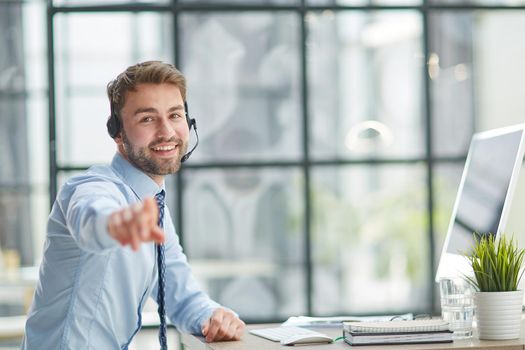 Young handsome male customer support phone operator with headset working in his office
