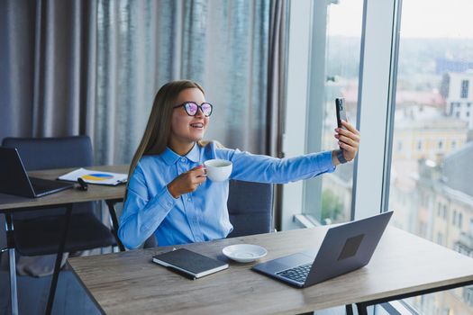 Smart female employee with netbook looking at camera during mobile call, successful freelancer in jacket talking on phone via app