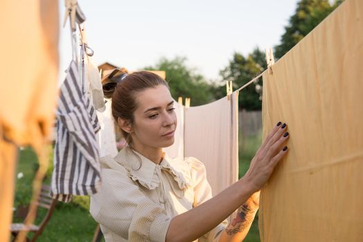 Laundry day. A woman hangs linen and towels on a tree in the courtyard of a village house. Summer cottage concept.