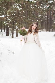 Beautiful bride in a white dress with a bouquet in a snow-covered winter forest. Portrait of the bride in nature.