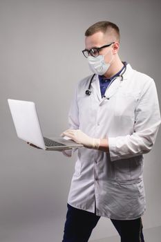 Young caucasian male doctor in uniform with a laptop for notes, on a gray background. Physician-therapist medical student. Medical education concept.