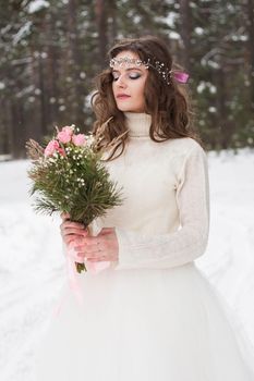 Beautiful bride in a white dress with a bouquet in a snow-covered winter forest. Portrait of the bride in nature.