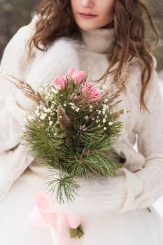 Beautiful bride in a white dress with a bouquet in a snow-covered winter forest. Portrait of the bride in nature.