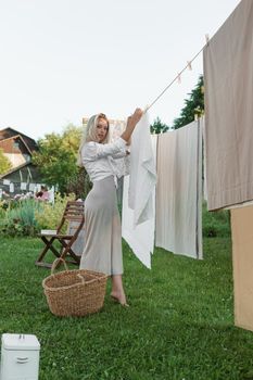 Laundry day. A woman hangs linen and towels on a tree in the courtyard of a village house. Summer cottage concept.