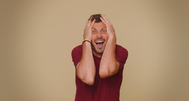 Scared fearful young man covering ears with hands, closing eyes, meeting own phobia, evidence horror event, screaming, shouting at loud, freaked out. Adult stylish guy on beige studio background