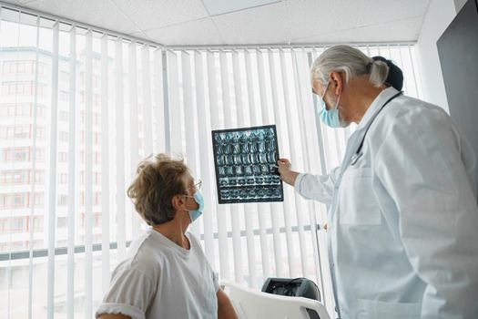 Doctor in mask explain to sick patient results of her MRI or X-Ray scan of spine. High quality photo