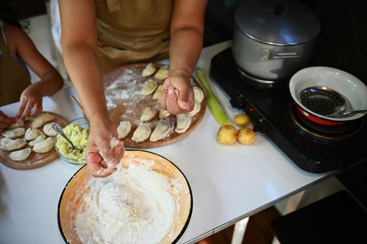 View from above of a female cook sprinkles while wholegrain flour on dough, to make homemade dumplings. Scene of artisanal food preparation. Russian pelmeni on a wooden board in the country kitchen