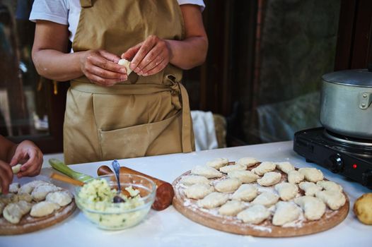 Cropped view of a woman, a housewife, cook in a beige chef's apron, making dumplings with potatoes. Ukrainian national dish- homemade Vareniki. Pelmeni. Baking concept. Traditional meal in Ukraine