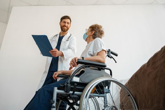 Doctor in uniform explaining to sick patient in wheelchair details of treatment. High quality photo