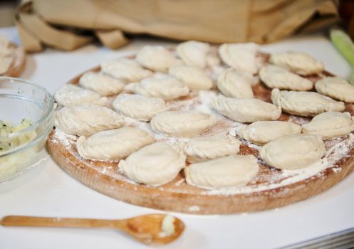 Selective focus on homemade dumplings, Ukrainian varenyky sprinkled with wholegrain flour, on wooden board, prepared according to traditional recipe. National dish in Ukraine. Russian Pelmeni. Ravioli