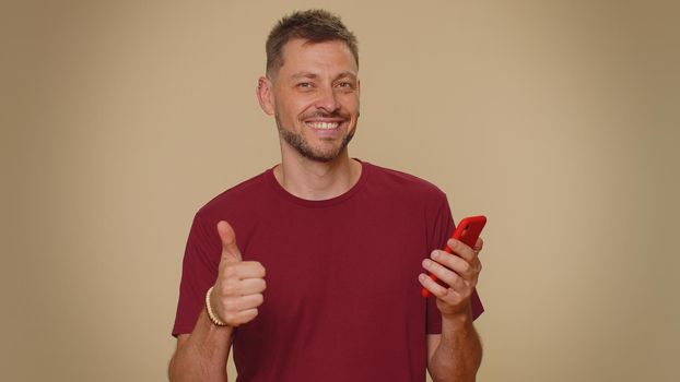Handsome young male man using smartphone typing new post on web, browsing, searching, addiction of social networks, show thumbs up like, positive feedback, recommends wifi cellular connection 5G