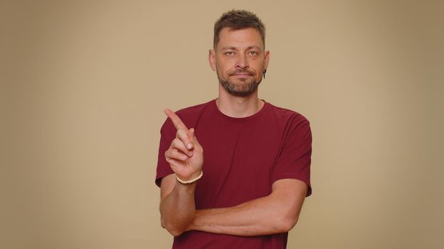 Offended handsome young man having misunderstanding, frustrated after quarrel, ignores and does not want to communicate, talk. Adult stylish male guy isolated on beige studio background indoors