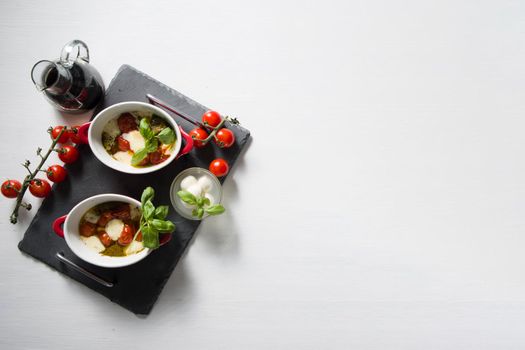 Italian caprese salad, baked cherry tomatoes, mozzarella and basil on a white table, still life, flat lay, copy space