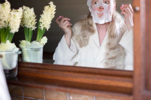 a middle-aged woman is busy with morning hygiene, trying in vain to straighten the mask with cleansing and moisturizing impregnation on her face High quality photo