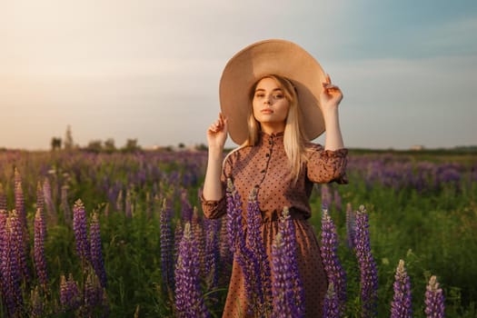 A beautiful woman in a straw hat walks in a field with purple flowers. A walk in nature in the lupin field.