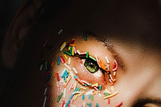 An open, green woman's eye with a sweet, multicolored sprinkle on the eyelid, around the eye