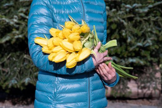 woman in a bright blue jacket with a bouquet of yellow spring tulips, mother's day gift. High quality photo