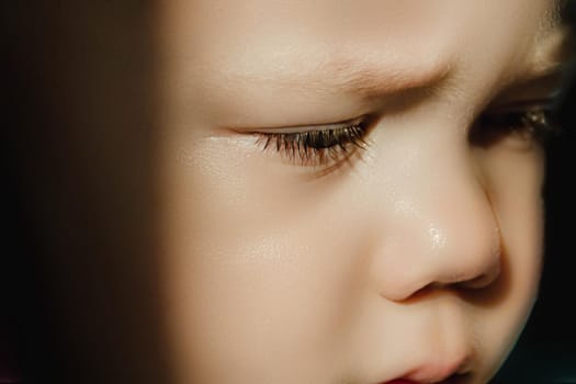 A small, sad boy with lowered gazes and eyelashes. Cute kid with frowning eyebrows