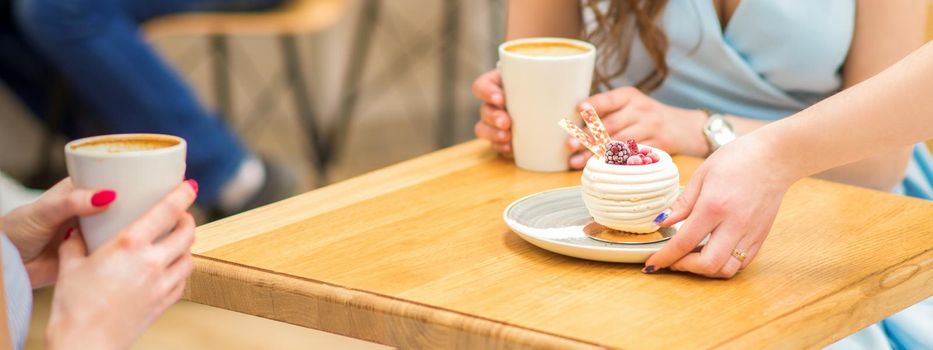 The waitress's hand puts the piece of cupcake on the table at a cafe, woman hand is putting round little pastry on the table on a background of a female in a blue dress